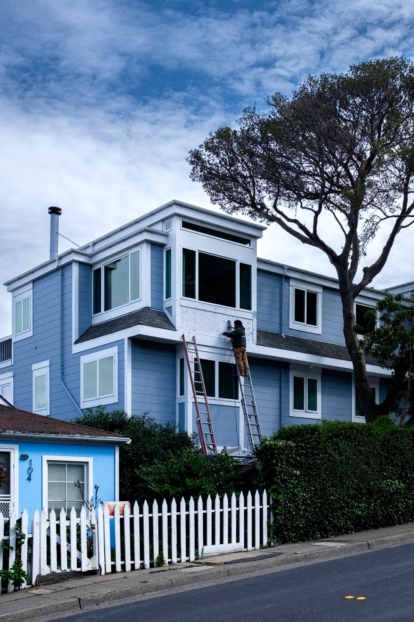 A man on a ladder repairing his house, accompanied by an empty ladder.